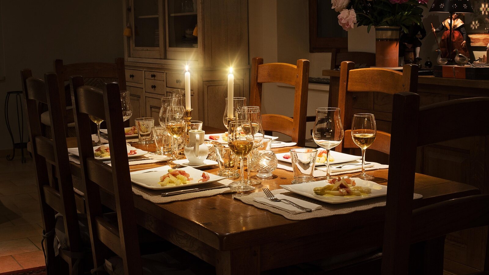 A candlelit dinner table set for guests, chairs still empty